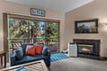 Relax in your cozy living room with a warm fireplace and natural light streaming through glass doors to a private deck surrounded by tall pines.