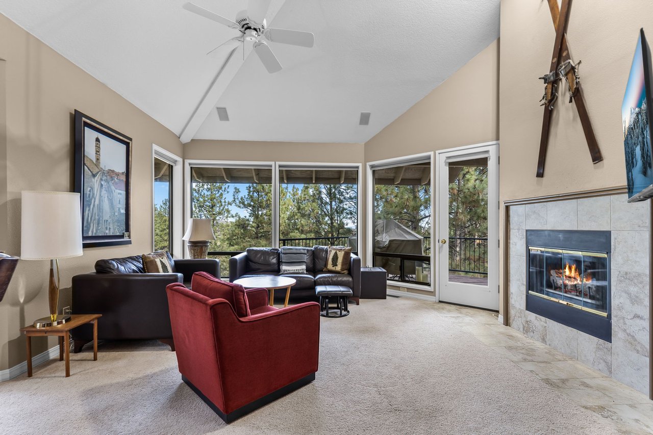Unwind in your spacious living room with cozy fireplace, comfortable seating, and panoramic tree views through floor-to-ceiling windows.