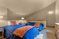 Rest easy in this cozy sleeping space, featuring twin beds dressed in plush blue and coral bedding, warm lighting, and a peaceful retreat under the eaves for your restful nights.