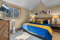 Unwind in your cozy bedroom with cheerful blue and gold bedding, warm wooden touches, and a view of towering pines right outside your window.