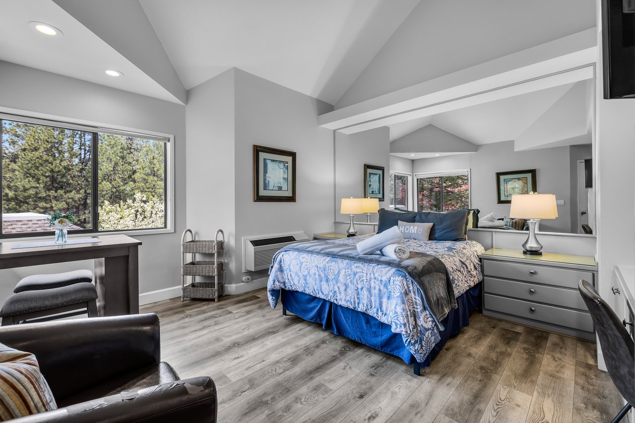 Step into your spacious bedroom retreat with high vaulted ceilings and natural light streaming through large windows. Unwind in style with cozy seating and a beautifully made bed inviting restful nights.